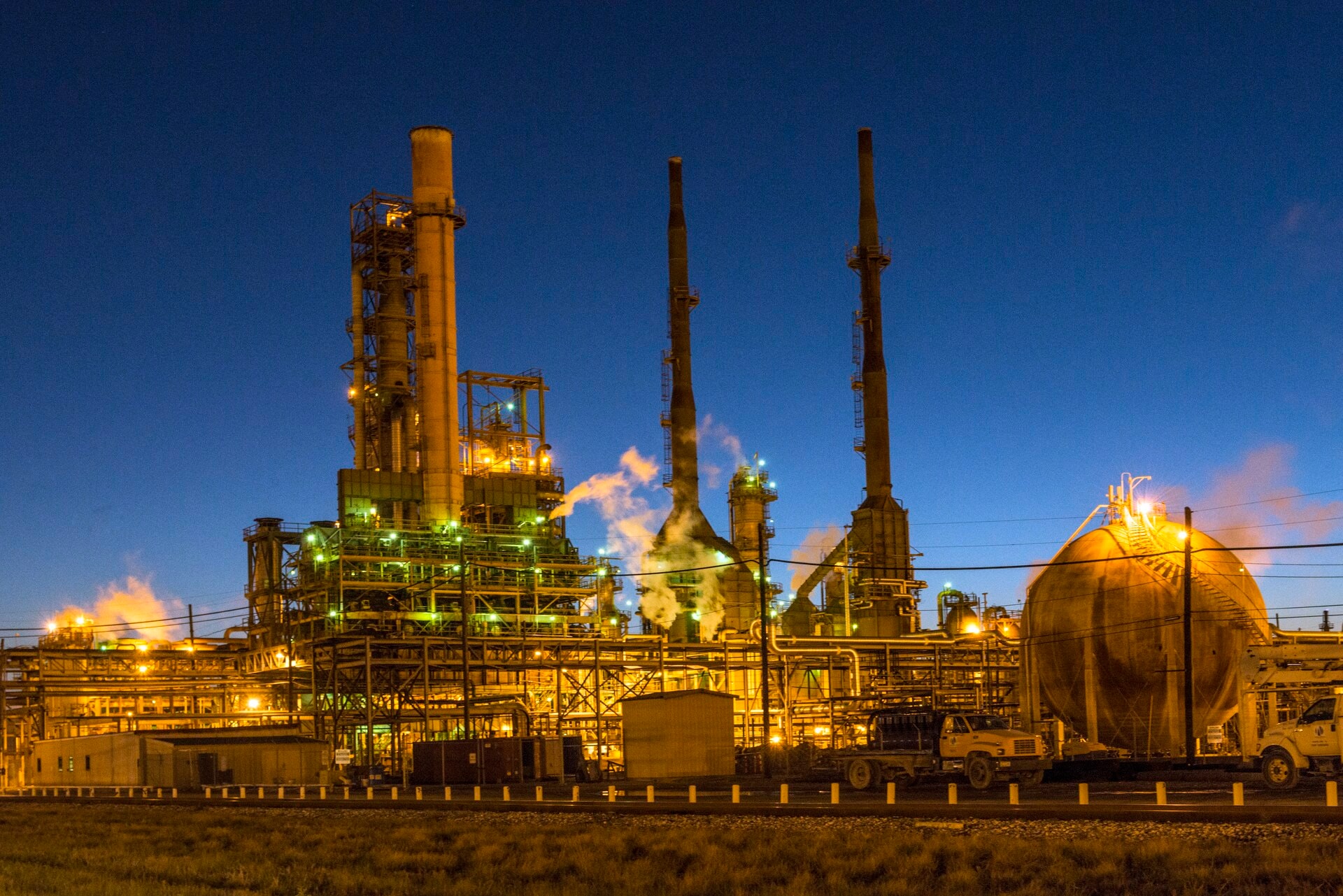 Oil refinery with distillation towers and storage tanks illuminated at dusk