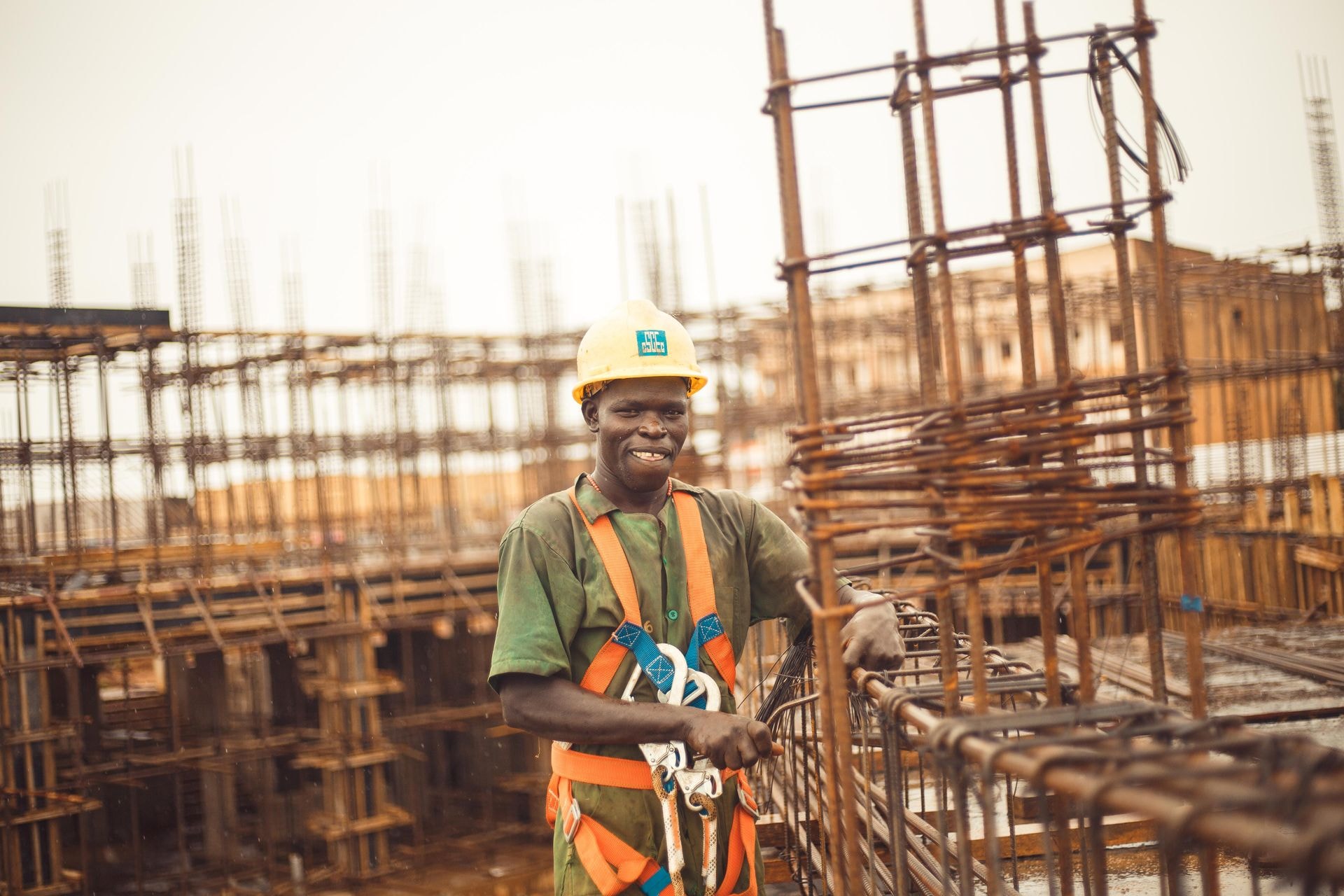 Smiling construction worker in a hard hat and safety harness among steel reinforcement on site