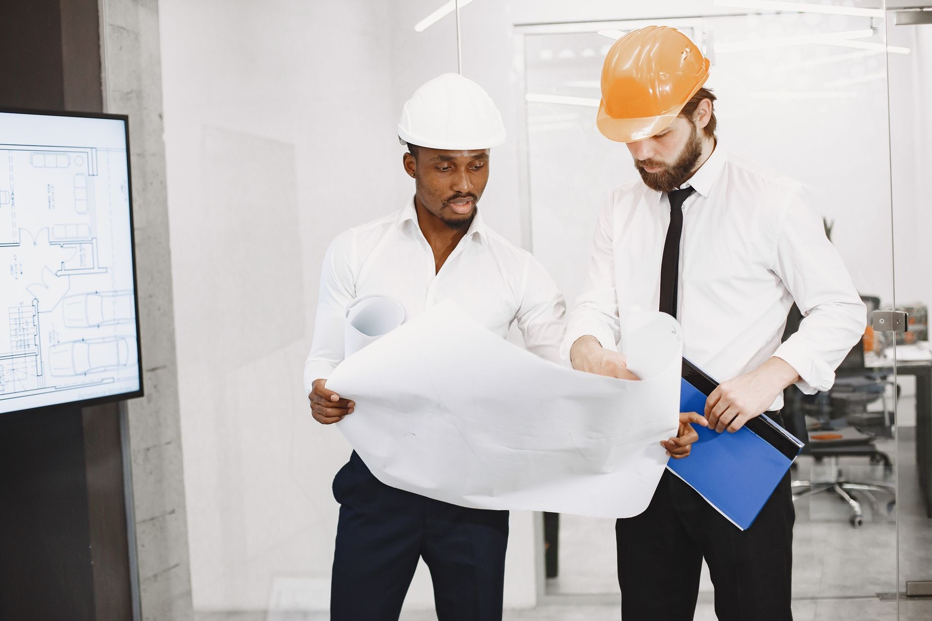 Two architects in hard hats reviewing a blueprint together